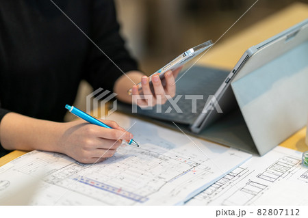 携帯を見ながら図面を書く女性一級建築士 82807112