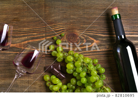 Red wine bottle, grape, chocolate and glasses over wooden table. Top view with copy space 82810695
