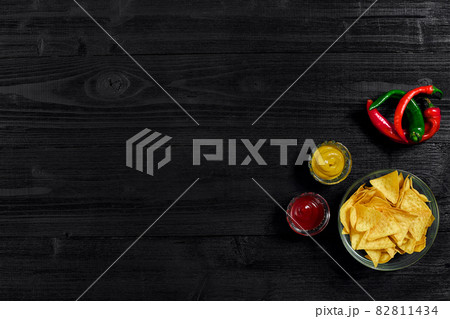 Glass plate with corn chips nachos and tomato sauce on a black wooden table top view. Place for text Glass plate with corn chips nachos and tomato sauce on a black wooden table top view. Place for text 82811434