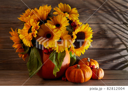 Autumn flowers composition in a pumpkin vase with pumpkins on wooden background Autumn flowers composition in a pumpkin vase with pumpkins on wooden background 82812004