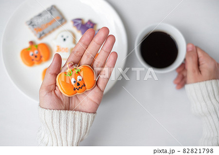 woman hand holding funny Halloween Cookie during drinking coffee. Happy Halloween day, Trick or Threat, Hello October, fall autumn, Traditional, party and holiday concept 82821798