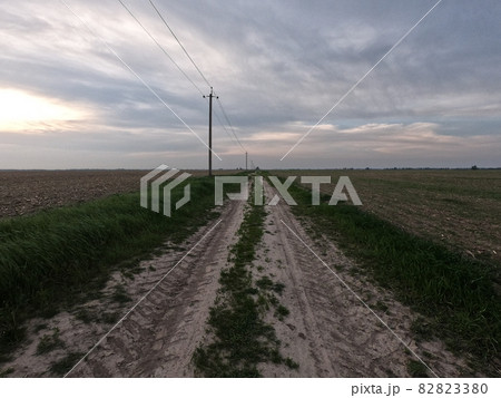 Dirt road among the field. A country road stretches into the distance among the fields. Evening landscape. Dirt road among the field. A country road stretches into the distance among the fields. Evening landscape. 82823380
