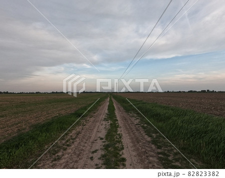 Dirt road among the field. A country road stretches into the distance among the fields. Evening landscape. Dirt road among the field. A country road stretches into the distance among the fields. Evening landscape. 82823382