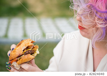 Caucasian woman with curly colored hair eating burger. Bad eating habits and love of fast food 82824040