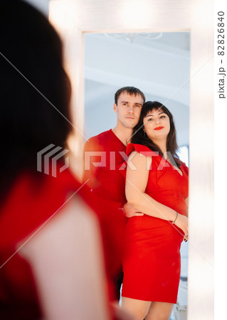 an attractive chubby woman in a red dress with a man looks in the mirror. an attractive chubby woman in a red dress with a man looks in the mirror. 82826840