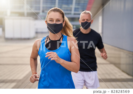 Motivated sportive woman wearing protective mask while running together with her husband to stay fit during Covid19 pandemic 82828569