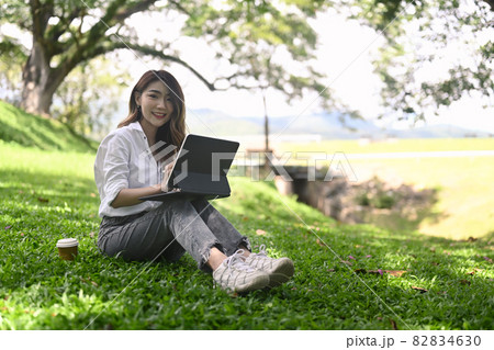Happy woman sitting on grass with computer laptop in public park. Happy woman sitting on grass with computer laptop in public park. 82834630