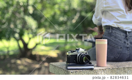 Retro camera, coffee cup and book on bench in nature park. 82834631