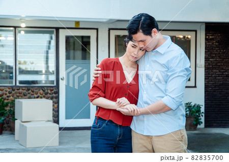 Man comforting his wife and woman hugging her husband and cry in front of the house and full of cardboard boxes during the transport in move out day, moving home concept Man comforting his wife and woman hugging her husband and cry in front of the house and full of cardboard boxes during the transport in move out day, moving home concept 82835700