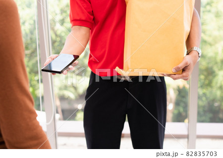 Asian delivery man holding holding a bag of fresh food for giving to customers and holding smartphone for Receive payments at home. Concept of express grocery service and new lifestyle 82835703