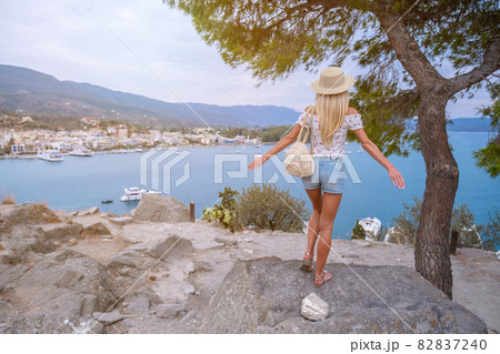 Beautiful girl tourist stands on a cliff overlooking the sea and the bay, Poros, Greece Beautiful girl tourist stands on a cliff overlooking the sea and the bay, Poros, Greece 82837240
