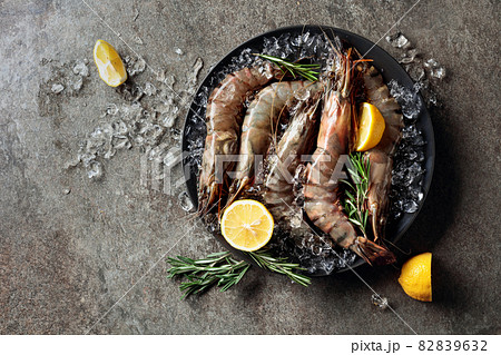 Fresh tiger prawns in a black plate with lemon, rosemary and crushed ice. 82839632