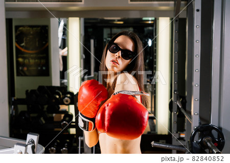 Seductive boxer model wearing big gloves and posing in fitness gym Seductive boxer model wearing big gloves and posing in fitness gym 82840852
