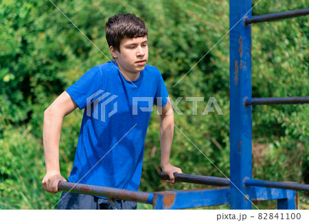teenage boy exercising outdoors, sports ground in the yard, he does push-ups at the bars, healthy lifestyle teenage boy exercising outdoors, sports ground in the yard, he does push-ups at the bars, healthy lifestyle 82841100