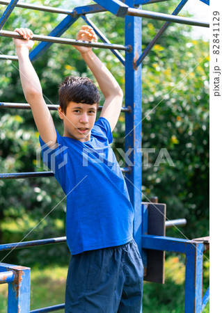 teenage boy exercising outdoors, sports ground in the yard, he pulls himself up on the horizontal bar, healthy lifestyle 82841129