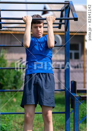 teenage boy exercising outdoors, sports ground in the yard, he pulls himself up on the horizontal bar, healthy lifestyle teenage boy exercising outdoors, sports ground in the yard, he pulls himself up on the horizontal bar, healthy lifestyle 82841142