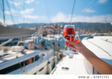 Woman holding glass of wine against yachts at the harbor of Poros. Greece 82841502