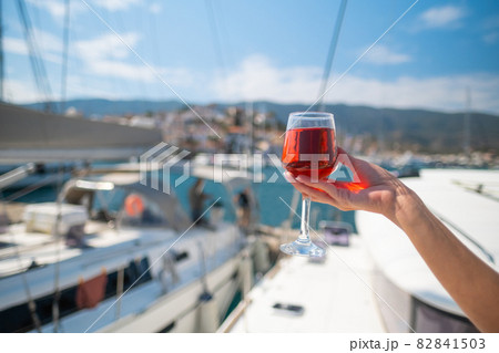 Woman holding glass of wine against yachts at the harbor of Poros. Greece Woman holding glass of wine against yachts at the harbor of Poros. Greece 82841503
