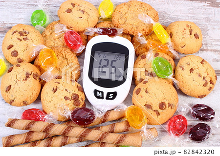 Glucometer with result sugar level and colorful candies with cookies, diabetes 82842320