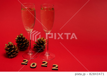 Studio shot of group of New year object, wooden 2022 numerals, golden pine cones and champagne flutes with sparkling wine isolated on red background with copy space. Merry Christmas concept Studio shot of group of New year object, wooden 2022 numerals, golden pine cones and champagne flutes with sparkling wine isolated on red background with copy space. Merry Christmas concept 82843471