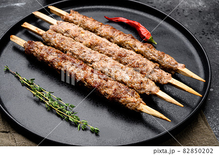 Shish kebab on a stick, from ground land mutton meat, on plate, on black dark stone table background Shish kebab on a stick, from ground land mutton meat, on plate, on black dark stone table background 82850202