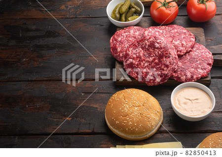 Raw Ground beef meat Burger steak cutlets and seasonings with buns, on old dark wooden table background, with copy space for text Raw Ground beef meat Burger steak cutlets and seasonings with buns, on old dark wooden table background, with copy space for text 82850413