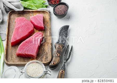 Raw tuna steak, fresh red tuna fillet with ingredients, green pea, sesame and spices, on wooden tray, on white stone background , with copyspace and space for text Raw tuna steak, fresh red tuna fillet with ingredients, green pea, sesame and spices, on wooden tray, on white stone background , with copyspace and space for text 82850481