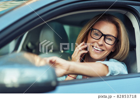 Portrait of successful happy business woman talking by mobile phone and smiling while driving a car, looking on the road through the window 82853718