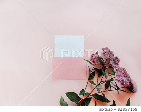 Pink envelope with a white mockup sheet and pink flowers next to it on pink background. 82857169