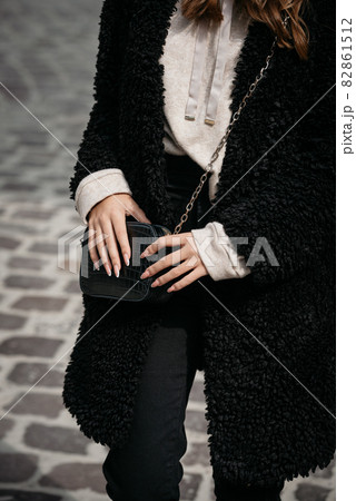 Close-up photo of young beautiful woman in black fur coat, jeanse and shoes posing on street 82861512