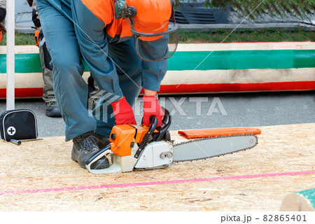 A man starts a chainsaw on a work site before a lumberjack competition. 82865401
