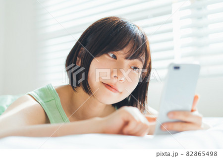 ベッドに寝転がってスマホを使う女性 82865498