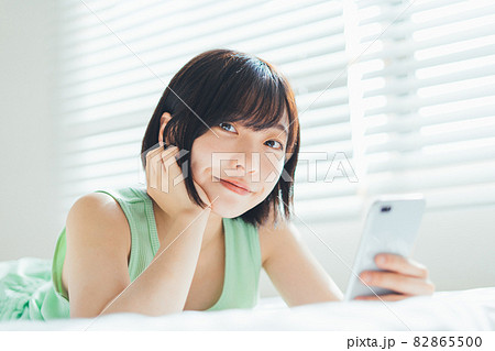 ベッドに寝転がってスマホを使う女性 82865500