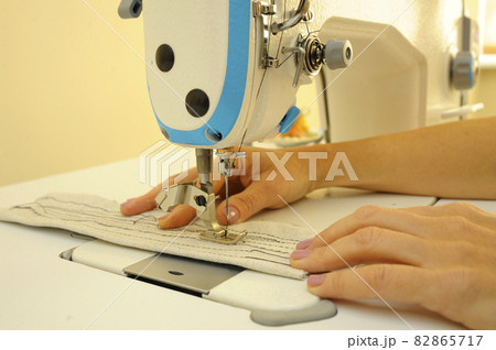 Seamstress hands sew on a sewing machine. Parts of sewing machine needle bar, presser foot, needle Plate, feed dog, needle with a thread threaded, piece of cloth Seamstress hands sew on a sewing machine. Parts of sewing machine needle bar, presser foot, needle Plate, feed dog, needle with a thread threaded, piece of cloth 82865717