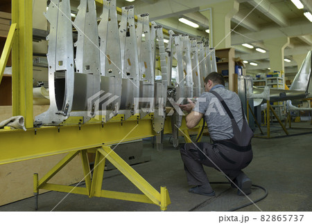 Worker working with a pneumatic drill assembling a fuselage of light plane at the assembly shop Worker working with a pneumatic drill assembling a fuselage of light plane at the assembly shop 82865737