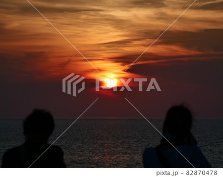 海に沈む夕日と夕焼けの空を見る2人の人影 海に沈む夕日と夕焼けの空を見る2人の人影 82870478