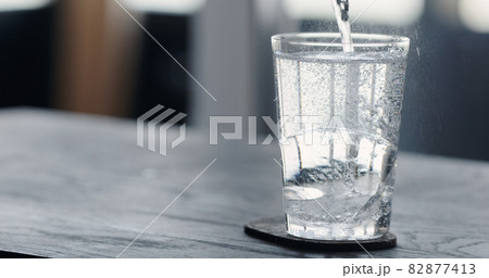 pour tonic water over clear ice ball in tumbler glass on black oak table pour tonic water over clear ice ball in tumbler glass on black oak table 82877413