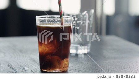 add straw to espresso tonic ice ball in tumbler glass on black wood table closeup 82878333