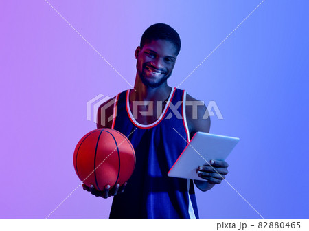 Portrait of professional player with basketball using tablet computer in neon lighting. Sports games concept 82880465
