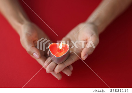 Red burning candle in the shape of a heart in female hands on red background 82881112