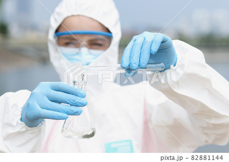 Scientist in protective suit with glasses pours water from test tube into flask Scientist in protective suit with glasses pours water from test tube into flask 82881144