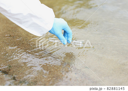 Hand of scientist in protective suit and glove makes water intake in lake Hand of scientist in protective suit and glove makes water intake in lake 82881145