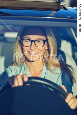 Cheerful beautiful mature woman or business lady wearing eyeglasses driving her modern car through the city on sunny day, she is looking on the road and smiling 82883755