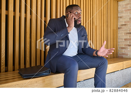 A dark-skinned businessman talking on the phone and looking involved 82884046