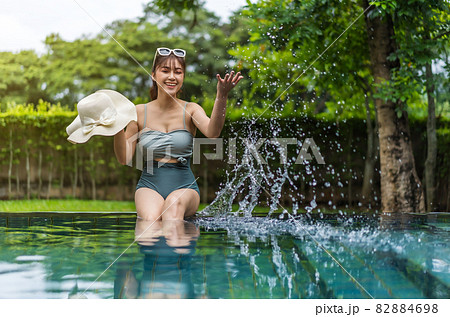 woman sitting on edge of swimming pool and playing water splashing woman sitting on edge of swimming pool and playing water splashing 82884698