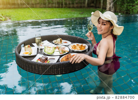 cheerful woman enjoying with floating food and champagne glass in swimming pool cheerful woman enjoying with floating food and champagne glass in swimming pool 82884700