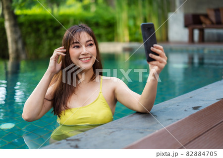 happy woman using smartphone to selfie a photo in swimming pool 82884705