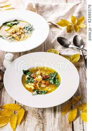 Vertical shot delicious autumn soup with chanterelles and fresh herbs. Seasonal dish with edible mushrooms. White plate and cutlery on a rustic background. Food still life. Organic wild foods. Vertical shot delicious autumn soup with chanterelles and fresh herbs. Seasonal dish with edible mushrooms. White plate and cutlery on a rustic background. Food still life. Organic wild foods. 82889376