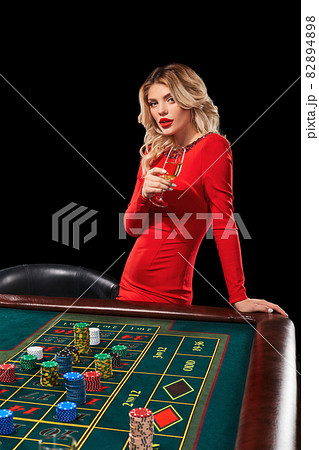 girl in a red dress with glass in his hand playing Roulette 82894898