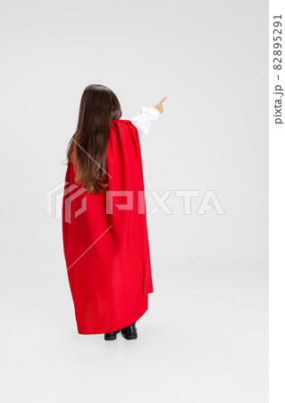Portrait of little girl wearing red cape standing isolated on white studio background with copyspace for ad. Back view 82895291